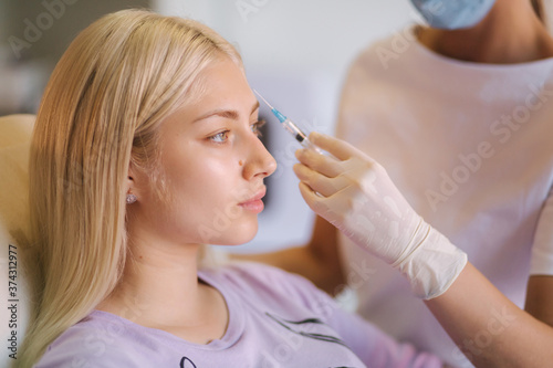 Hands of cosmetologist making injection in face  lips. Young woman gets beauty facial injections in medical clinic