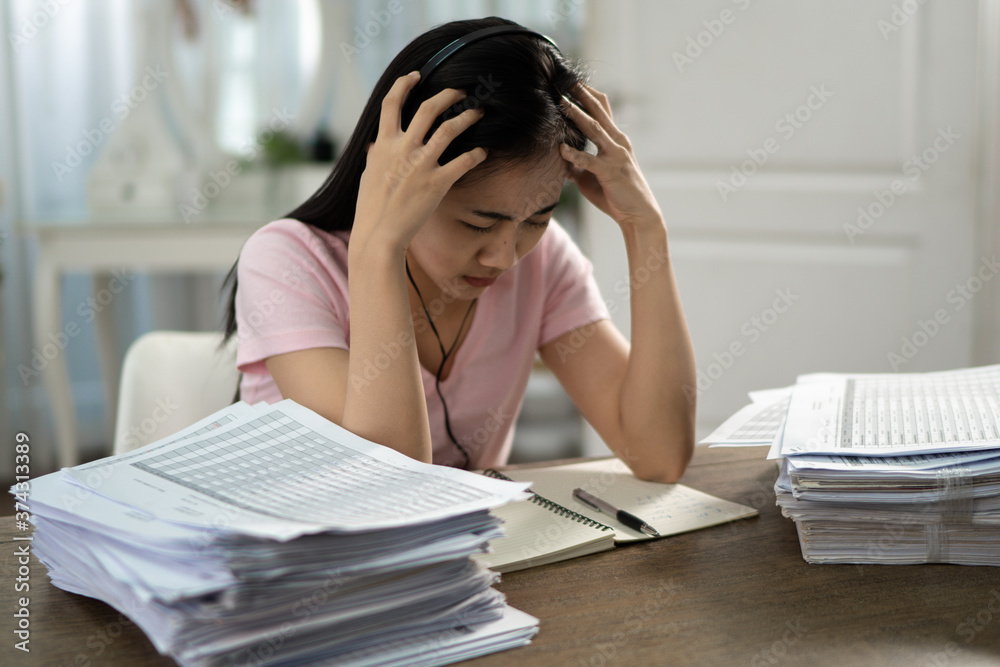 A beautiful Asian woman wearing a pink shirt and headphones is crying over an online class in her home.. A beautiful Asian woman wearing a pink shirt and headphones is crying over an online class in her home..