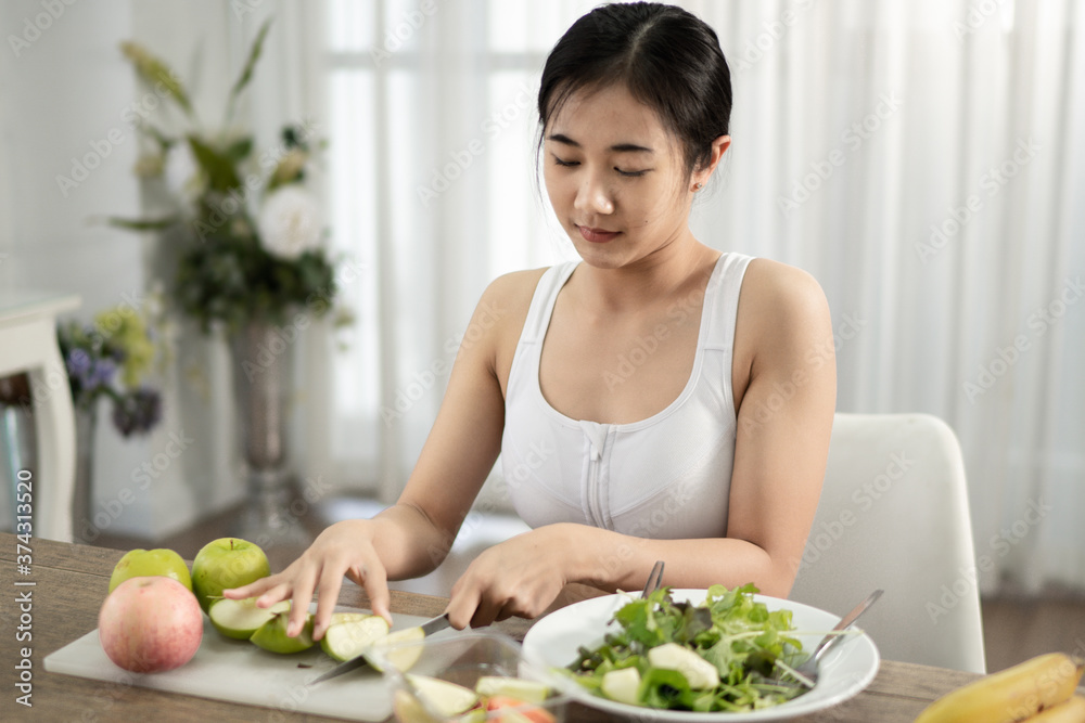A healthy, healthy Asian woman uses a fruit knife to make a salad to eat inside her home. Healthy weight loss ideas.