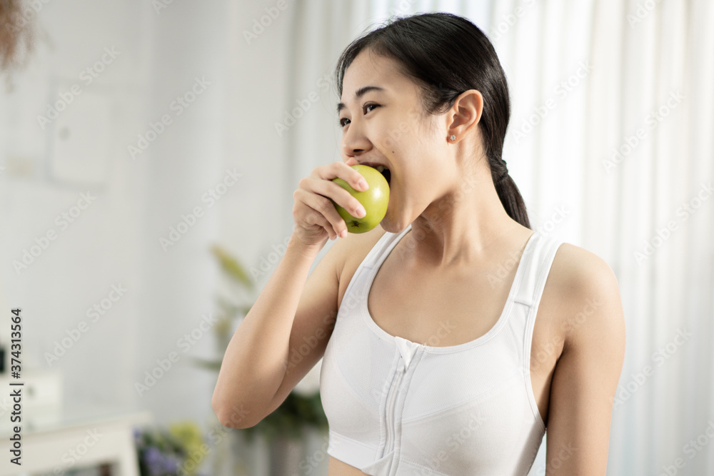 A pretty healthy Asian woman is eating green apple inside her home. Healthy weight loss ideas. A pretty healthy Asian woman is eating green apple inside her home. Healthy weight loss ideas.