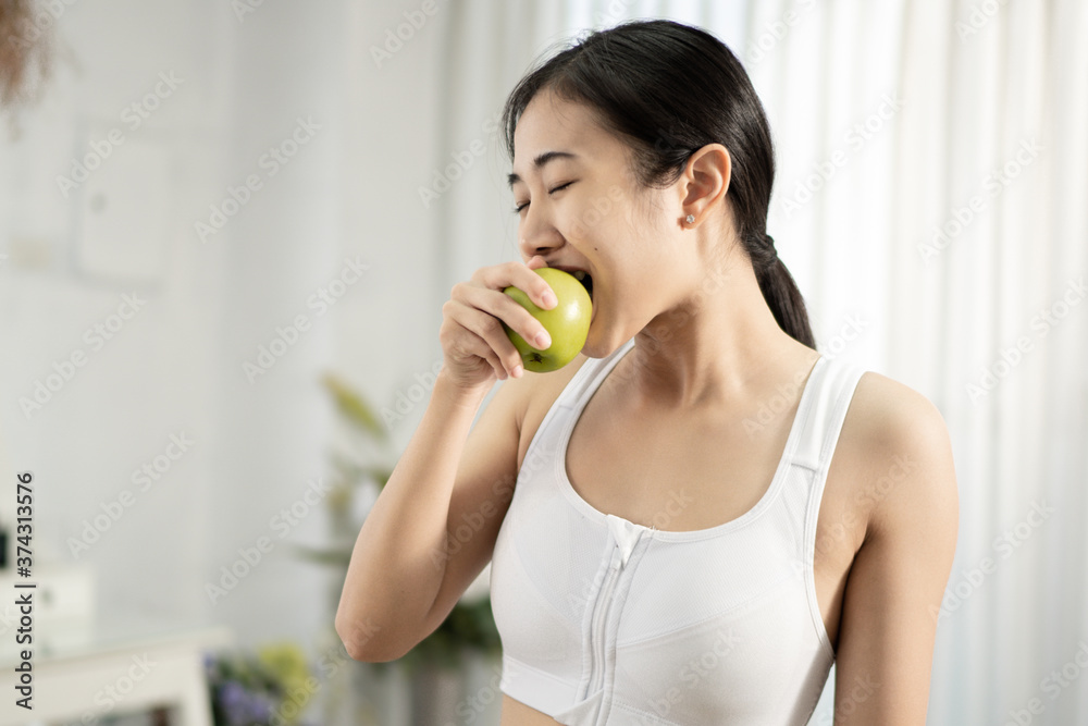 A pretty healthy Asian woman is eating green apple inside her home. Healthy weight loss ideas. A pretty healthy Asian woman is eating green apple inside her home. Healthy weight loss ideas.