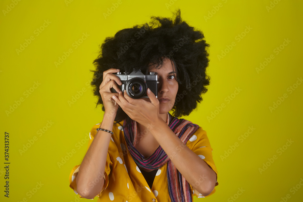 Beautiful indian girl with afro curly hairstyle talking pictures with retro camera Beautiful indian girl with afro curly hairstyle talking pictures with retro camera