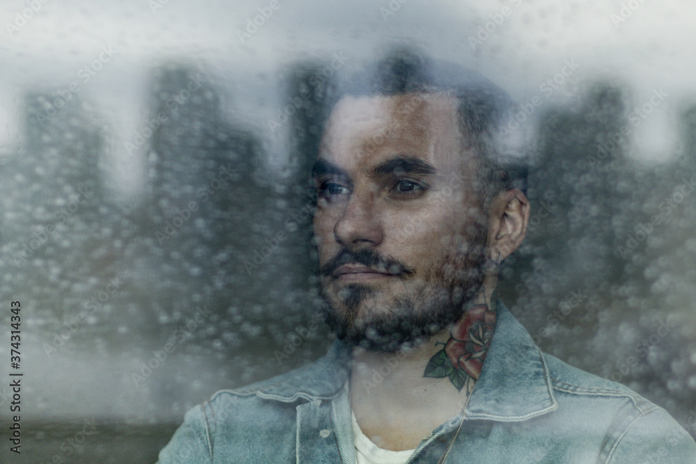 Young adult bearded male looking out of window on rainy day Young adult bearded male looking out of window on rainy day