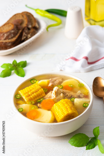 Delicious hearty lunch, soup with chicken and rice, sweet boiled corn ,green onions and potato in a plate on the table with bread, beautiful bouquet of flowers in a vase