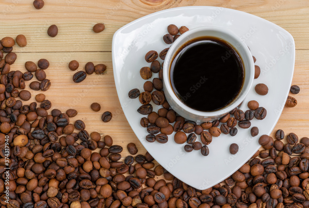 Espresso black coffee in a white cup with roasted coffee beans on wooden surface Espresso black coffee in a white cup with roasted coffee beans on wooden surface