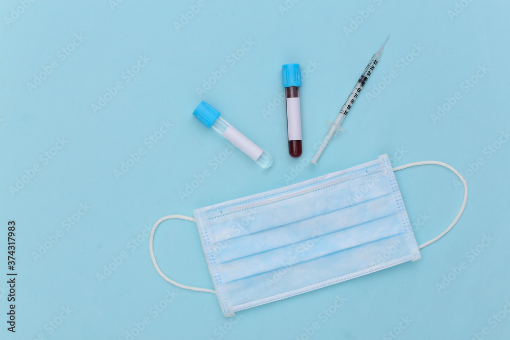 Blood test. Test tubes with syringe, medical mask on blue background. Top view Blood test. Test tubes with syringe, medical mask on blue background. Top view