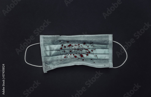 Facial medical mask with blood on a black background. Pandemic covid-19, pneumonia or tuberculosis. Top view photo