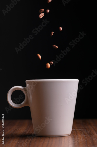 Mugful of coffee in white cup with coffee grains falling in it