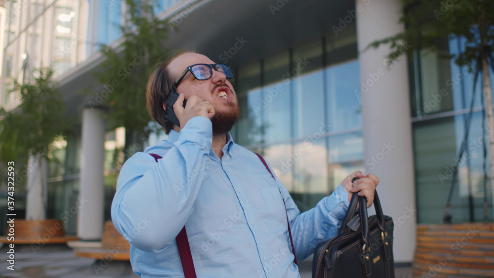 Young fat businessman arguing with client on smartphone walking in street Young fat businessman arguing with client on smartphone walking in street