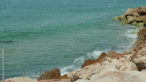 Wide shot of blue and green waves of a beautiful sea crushing onto stones of a sea shore. Slow motion 4K