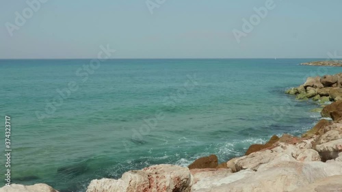 Wide shot of blue and green waves of a beautiful sea crushing onto stones of a sea shore. Slow motion 4K
