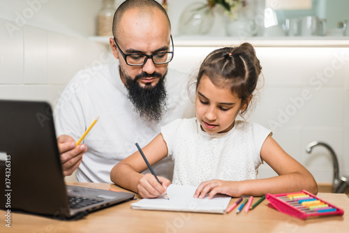Young father checking homework helping cute school child daughter with studies sit at kitchen table.