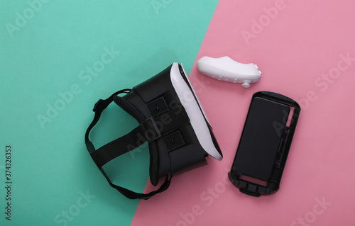 Virtual reality headset with joystick and smartphone on pink blue pastel background. Modern gadgets. Top view