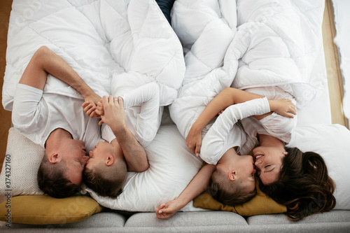 Young family enjoying in bed. Happy parents with sons relaxing in bed.