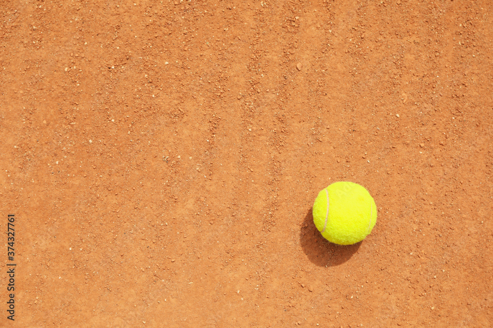 Light green tennis ball on clay court, space for text