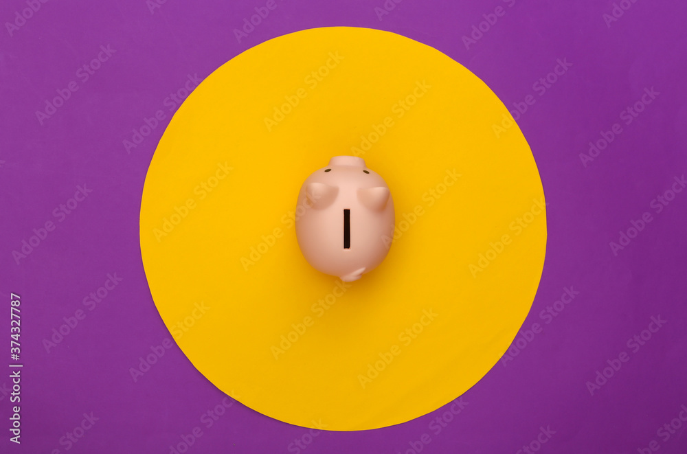 Piggy bank on purple background with yellow circle. Conceptual studio shot. Minimalism. Top view Piggy bank on purple background with yellow circle. Conceptual studio shot. Minimalism. Top view