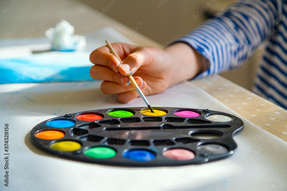Little kid painting with watercolor paint at home school. Close up of hand dipping brush into colourful paint. Creativity and stay at home concept Little kid painting with watercolor paint at home school. Close up of hand dipping brush into colourful paint. Creativity and stay at home concept