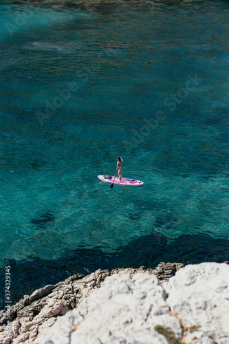 A woman is enjoying a session on a stand up paddle SUP on crystal clear waters in the South of France in Summer