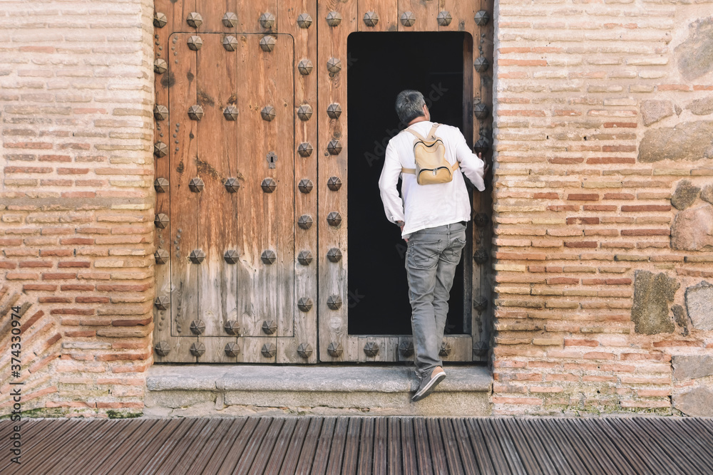 A middle aged man with a backpack looks out through an old open traditional wooden door. Rural and proximity tourism concept A middle aged man with a backpack looks out through an old open traditional wooden door. Rural and proximity tourism concept