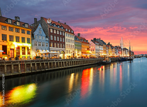Rows of bars, cafes and restaurants along the Nyhavn Canal illuminated at dusk in Copenhagen