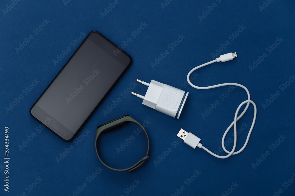 Modern gadgets. Smartphone, charging device, smart bracelet on classic blue background. Color 2020. Top view Modern gadgets. Smartphone, charging device, smart bracelet on classic blue background. Color 2020. Top view