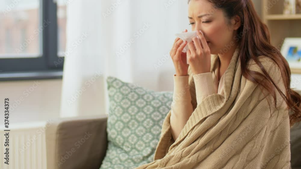 healthcare, cold, hygiene and people concept - sick asian woman in blanket taking paper tissue from box and blowing her nose at home healthcare, cold, hygiene and people concept - sick asian woman in blanket taking paper tissue from box and blowing her nose at home