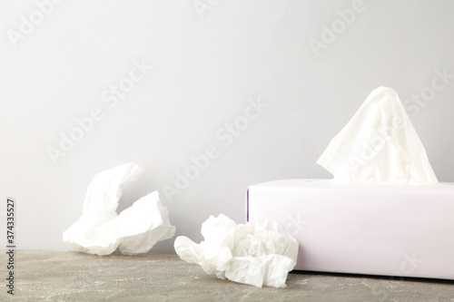 Box with paper tissues and used crumpled napkins on grey background