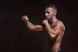 Charismatic athletic male fighter with muscular torso ready to strike isolated on dark background.