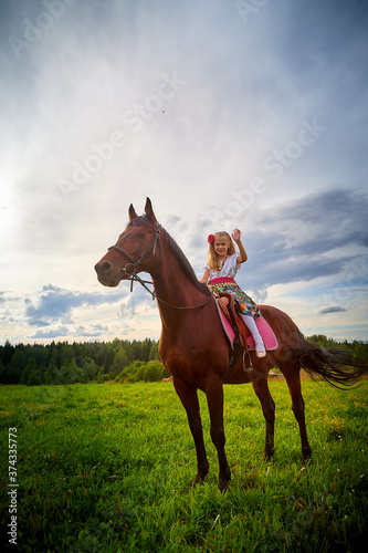 Girl in nice Gypsy dress with sorrel horse in a field with green grass and sky with clouds in background