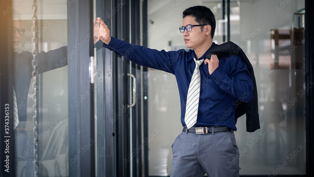 A young businessman wearing an Asian crowd is looking out at the glass window and his shadow. A young businessman wearing an Asian crowd is looking out at the glass window and his shadow.