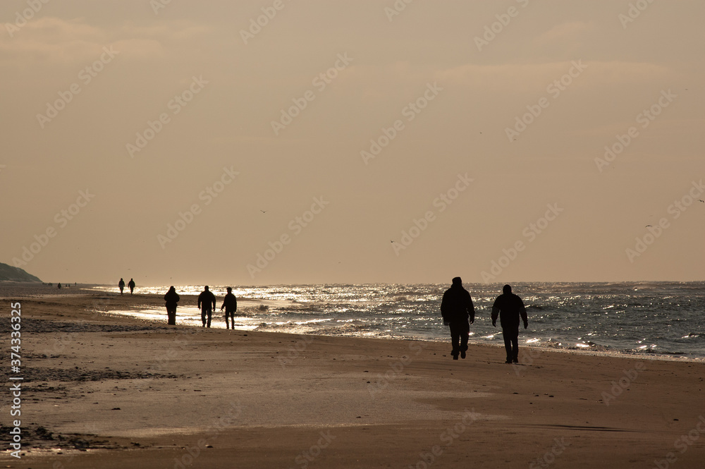 People on a beach walk in backlight at golden sunset on the North Sea in Denmark