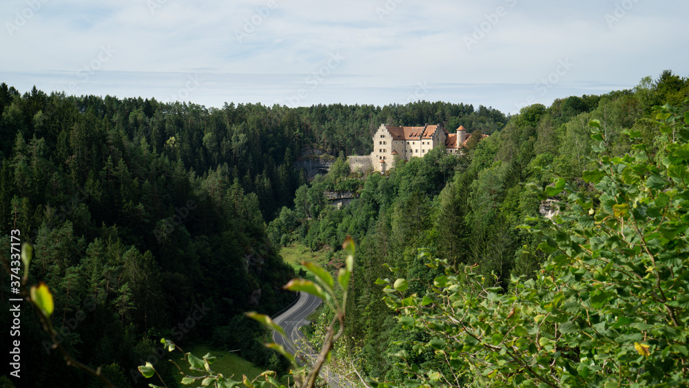 Landschaftspanorama rund um die Burg Rabenstein in der Fränkischen Schweiz nahe der A9 bei Tag. Wald aus Nadelbäumen mit einer Burg als Motiv bei blauem Himmel und Tageslicht. Bayern, Deutschland.