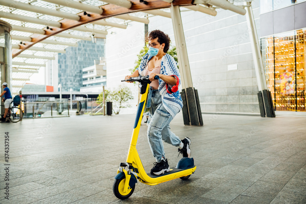 Young woman wearing mask riding kick scooter - Multiethnic female ecologist using e-scooter - green transportation, electric mobility, ecology concept Young woman wearing mask riding kick scooter - Multiethnic female ecologist using e-scooter - green transportation, electric mobility, ecology concept
