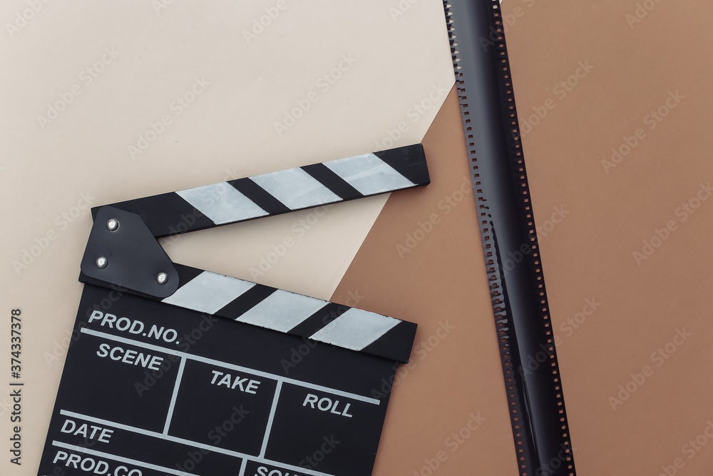 Movie clapper board with film tape on beige brown background. Filmmaking, Movie production, Entertainment industry. Top view