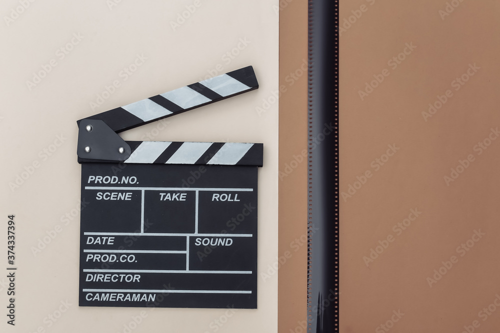 Movie clapper board with film tape on beige brown background. Filmmaking, Movie production, Entertainment industry. Top view