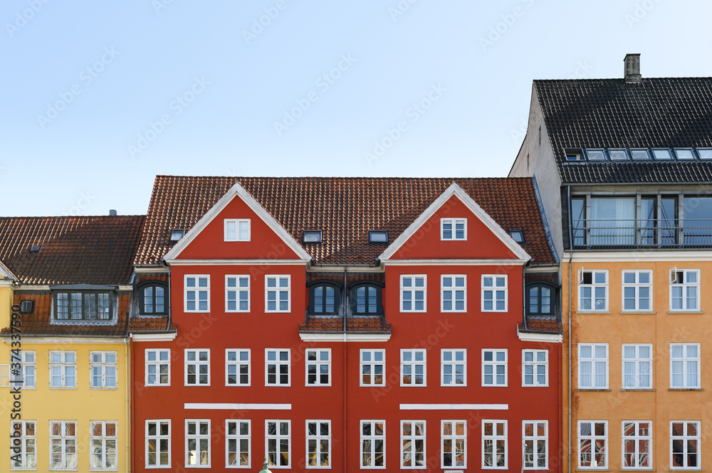 Colorful houses in yellow, red and orange of the Nyhaven in Copenhagen Denmark photographed frontally on a sunny day with a bright blue sky.