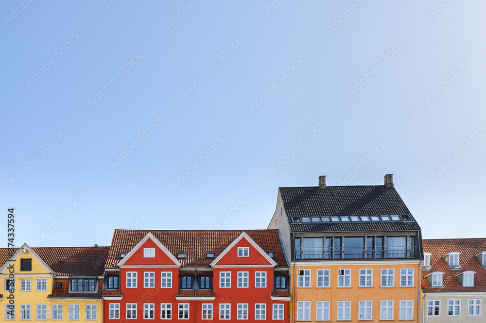 Colorful houses in yellow, red and orange of the Nyhaven in Copenhagen Denmark photographed frontally on a sunny day with a bright blue sky.