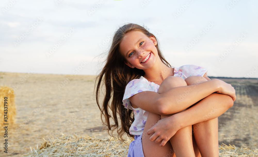 Adorable happy smiling ittle girl child sitting on a hay rolls in a wheat field Adorable happy smiling ittle girl child sitting on a hay rolls in a wheat field