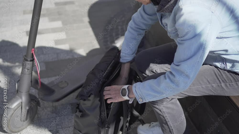 Hands of elderly woman wearing casual clothes takes out computer from backpack for remote work. Work outside concept. Middle age female in stylish jeans unpacks computer after riding electric scooter Hands of elderly woman wearing casual clothes takes out computer from backpack for remote work. Work outside concept. Middle age female in stylish jeans unpacks computer after riding electric scooter