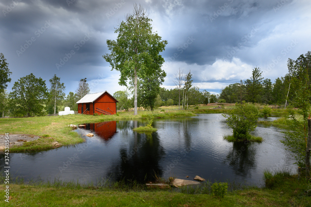 Obraz premium Small red Swedish house reflected in a small lake under a dramatic sky.