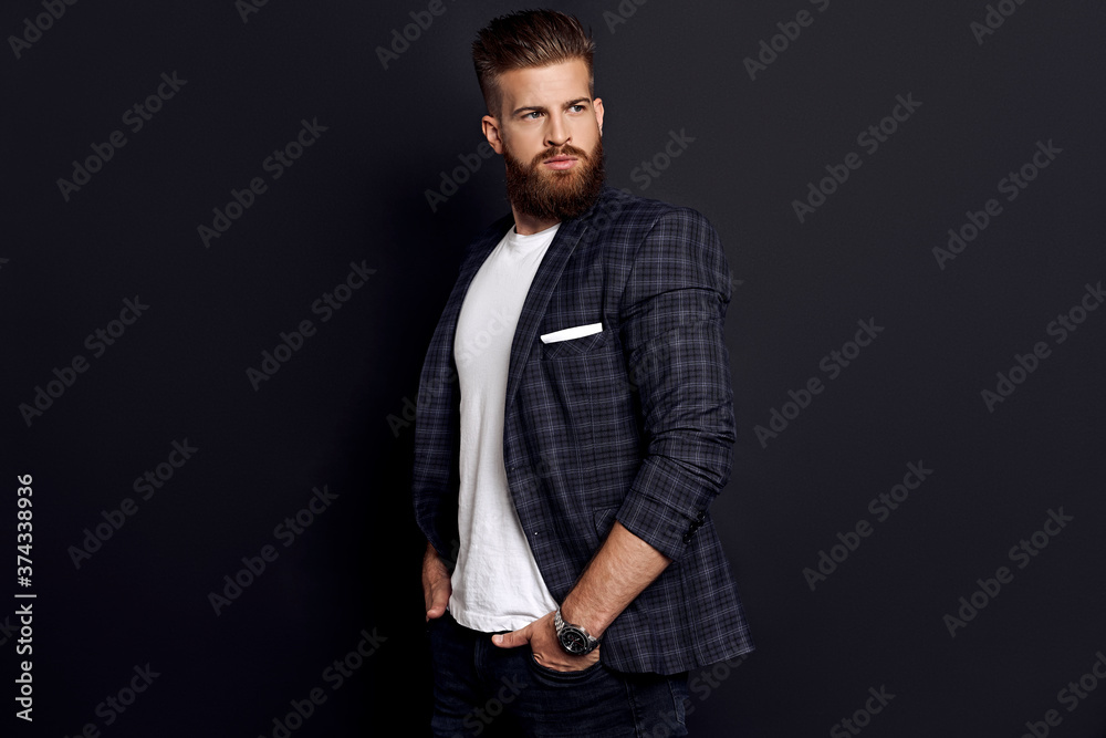 Handsome man with perfect hairdo and beard looking away while standing against black background