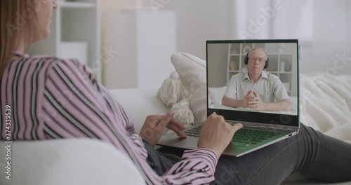 young woman is communicating with elderly male psychologist by video call, viewing screen of laptop, staying home photo