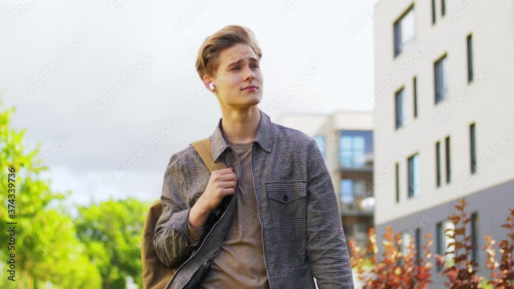 technology, leisure and people concept - young man or teenage boy with earphones and backpack walking in city technology, leisure and people concept - young man or teenage boy with earphones and backpack walking in city