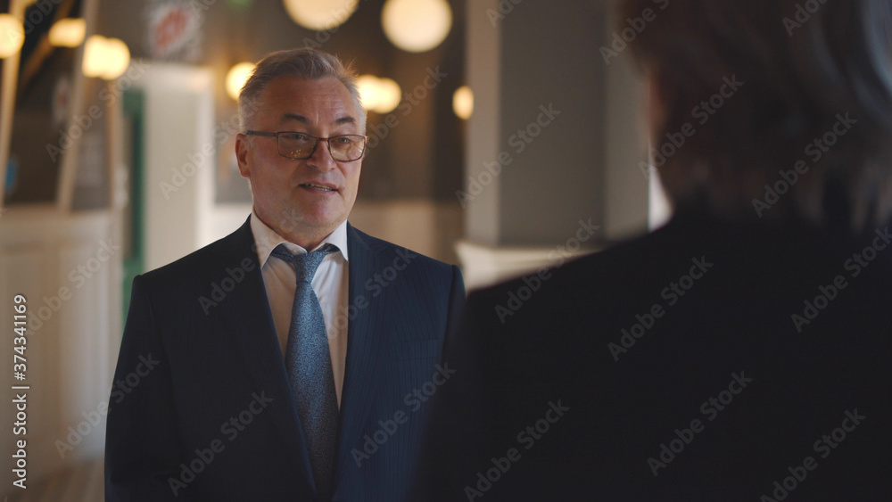 Fototapeta premium Back view of successful senior businessman talking to partner while waiting in lobby