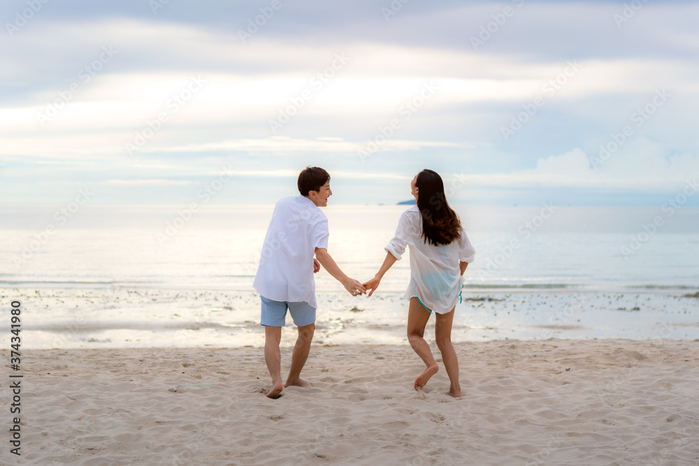 Asian couple in love having romantic tender moments running and hand hold on the beach between sunset in Thailand..