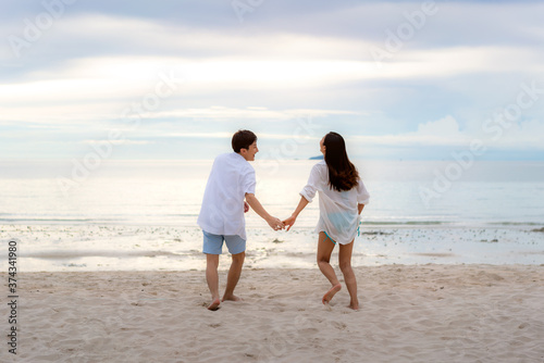 Asian couple in love having romantic tender moments running and hand hold on the beach between sunset in Thailand..