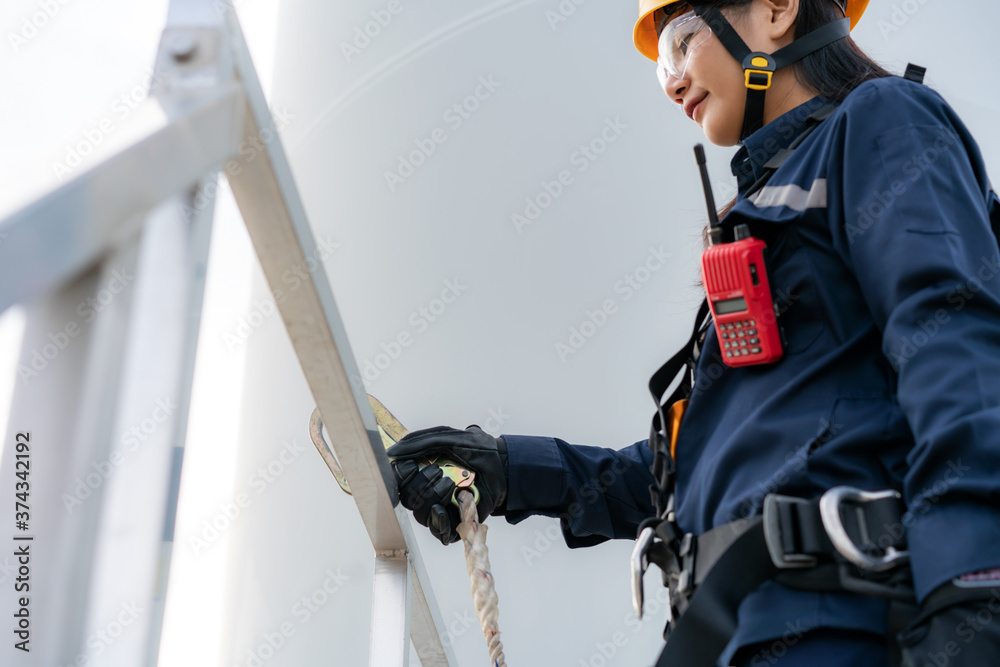 Fototapeta premium Asian woman Inspection engineer wearing safety harness and safety line working preparing and progress check of a wind turbine with safety in wind farm in Thailand.