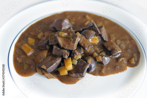 ready to eat, liver, heart and kidneys from a roe buck in sour sauce with onoins and apple on a white plate photo