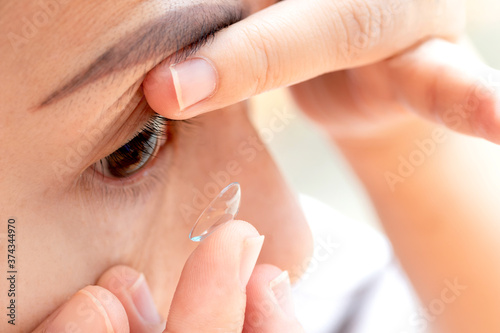 Close up young woman wearing contact lens. asian woman putting eye lenses with hands photo