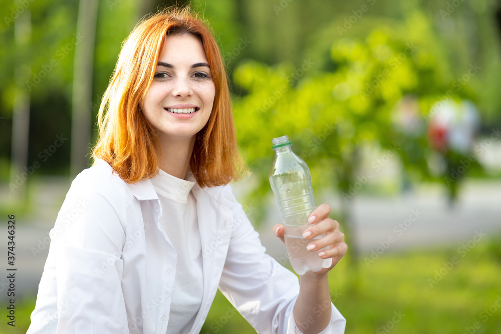 Young redhaired woman drinking water from a bottle on summer day. Young redhaired woman drinking water from a bottle on summer day.